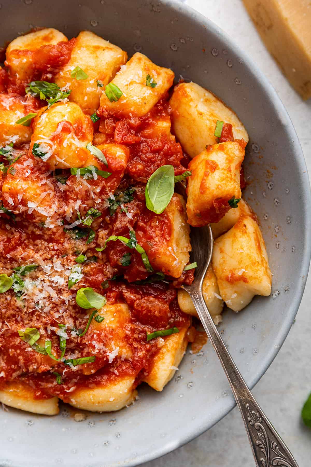 Potato gnocchi in bowl garnished with basil and cheese.