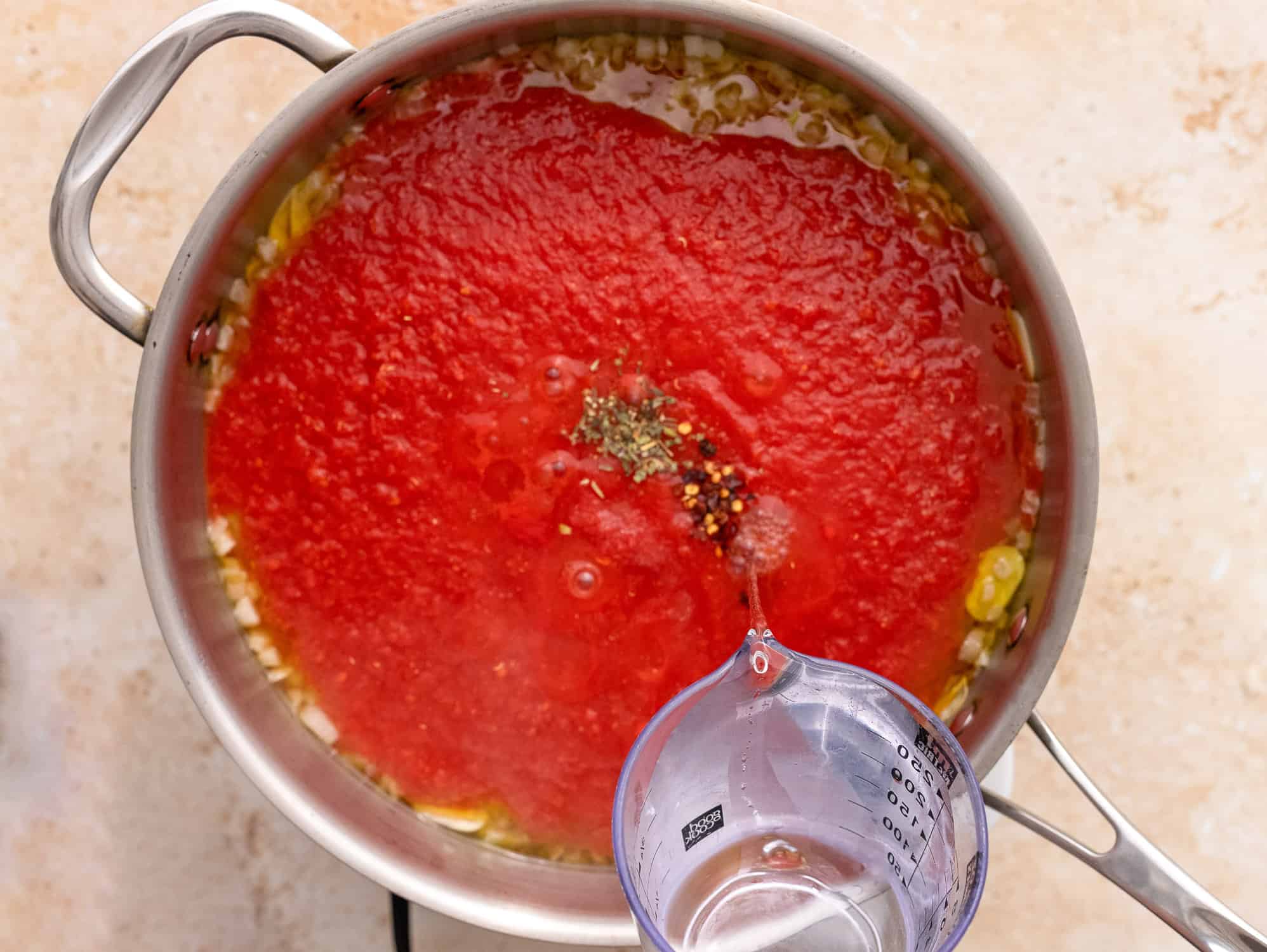 Pouring water into pan with aromatics and tomatoes. 