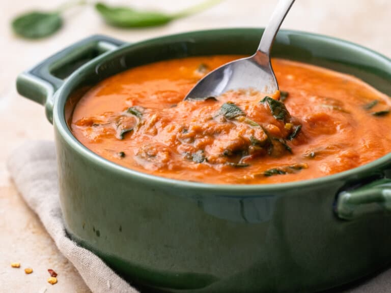 Side view of tomato florentine soup with spoon.