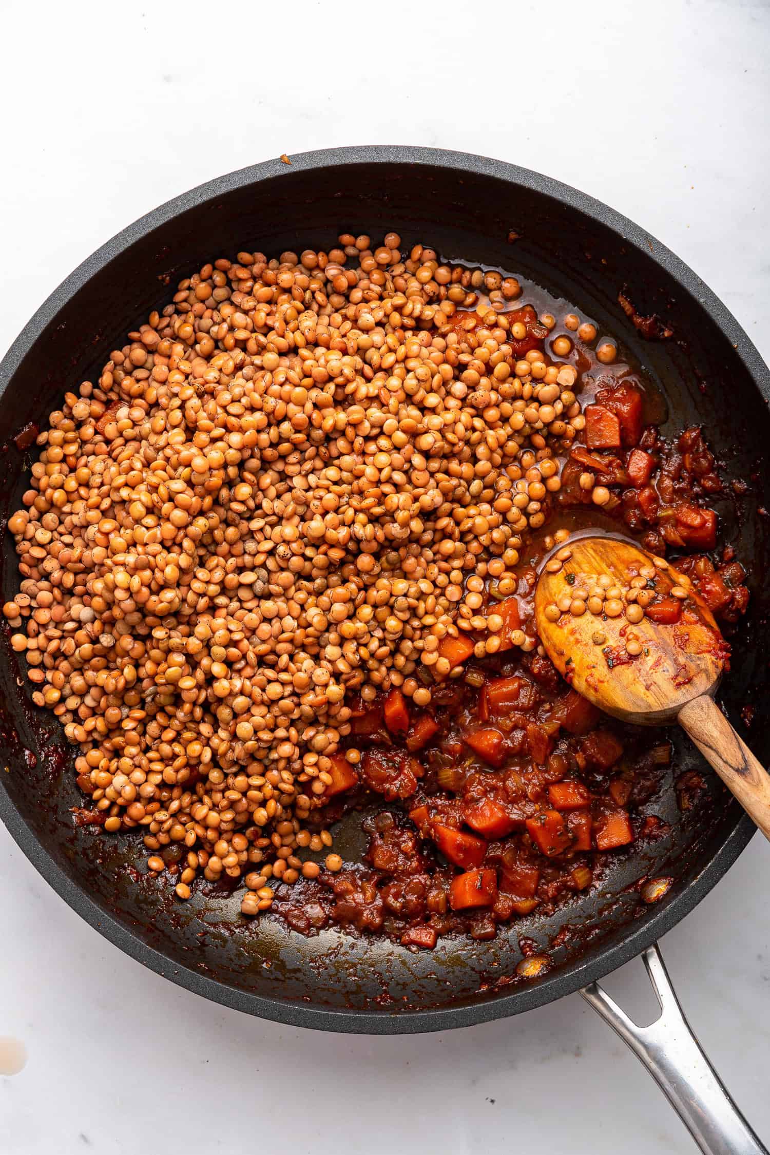 Adding lentils to skillet with mirepoix and tomato paste and herbs. 