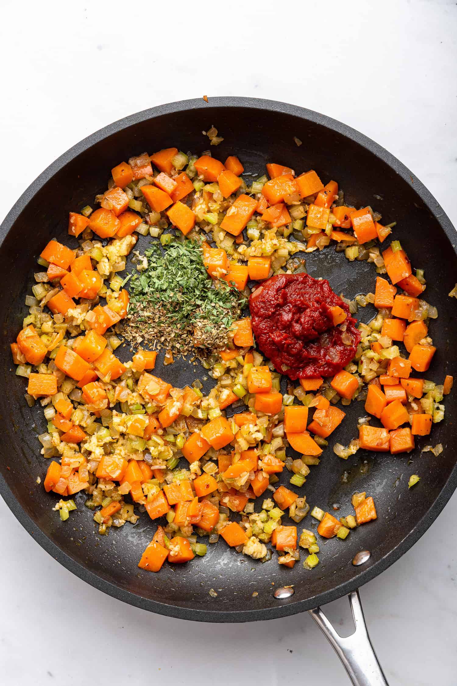 Adding tomato paste and herbs to pan with sautéed mirepoix.  