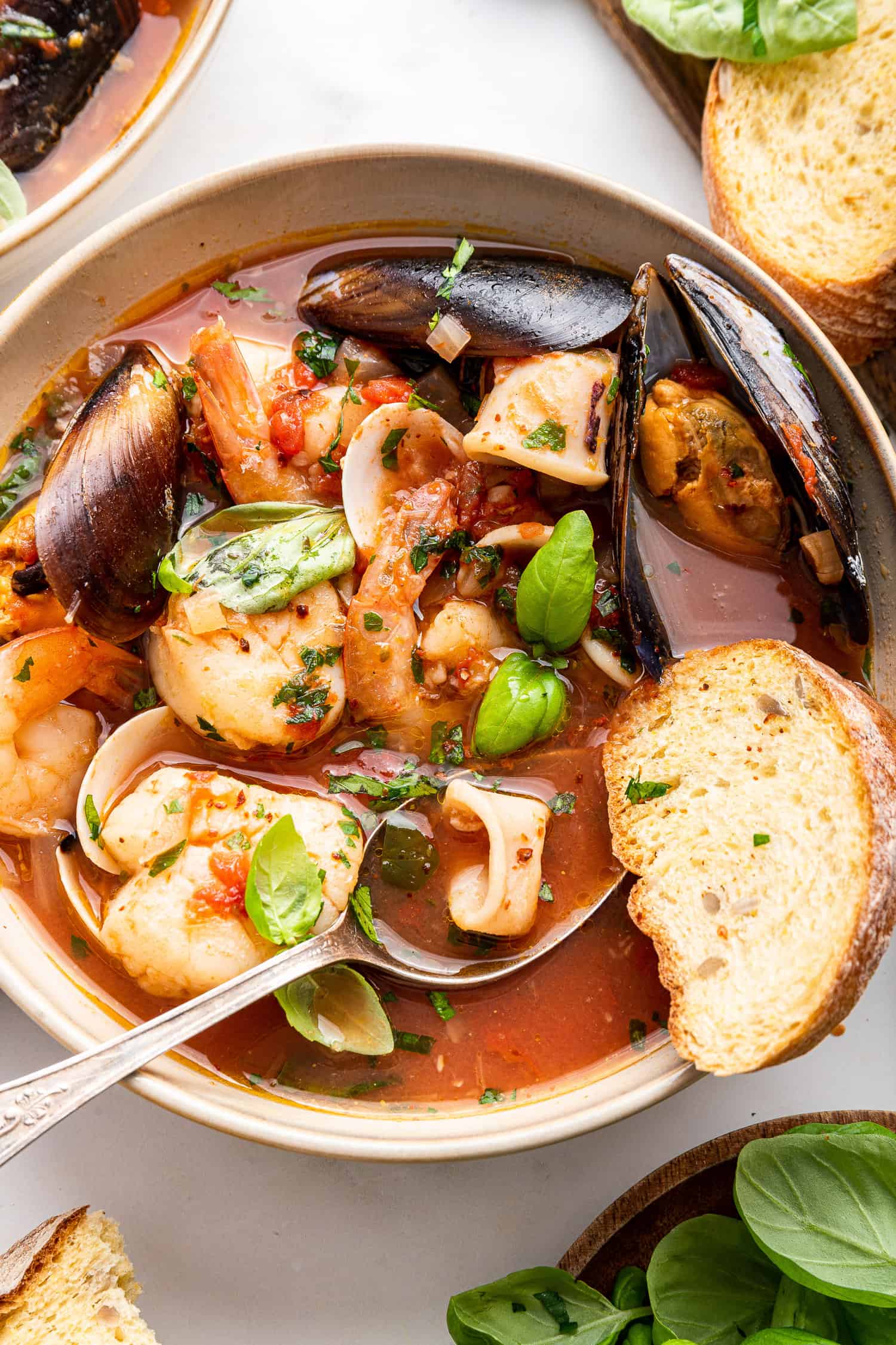 Zuppa di pesce with bread and spoon in bowl.