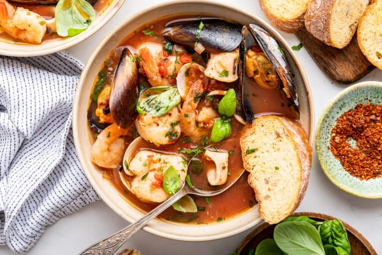 Zuppa di pesce in white pot with herbs and bread.
