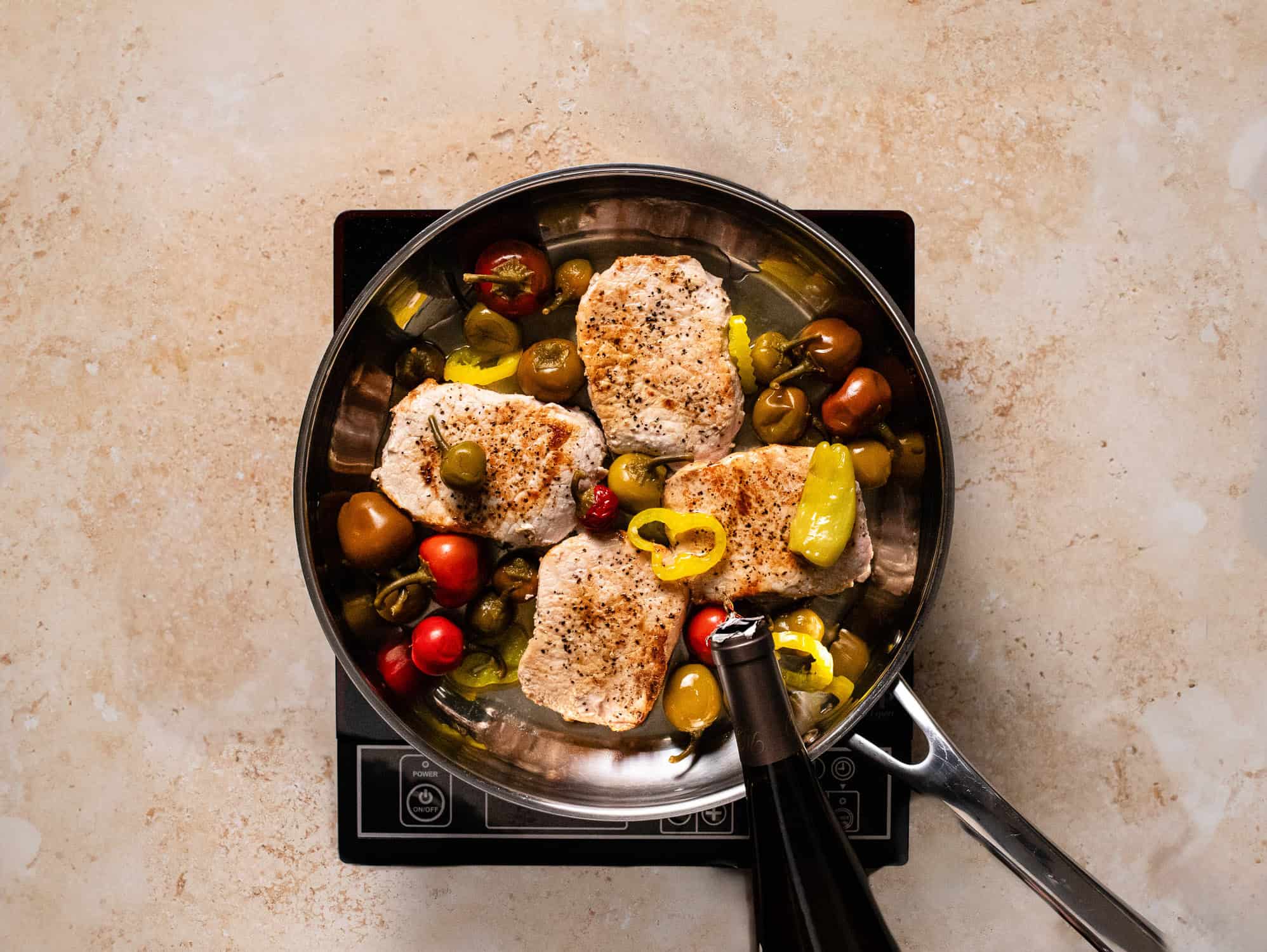 Pouring wine into pork and peppers in pan.