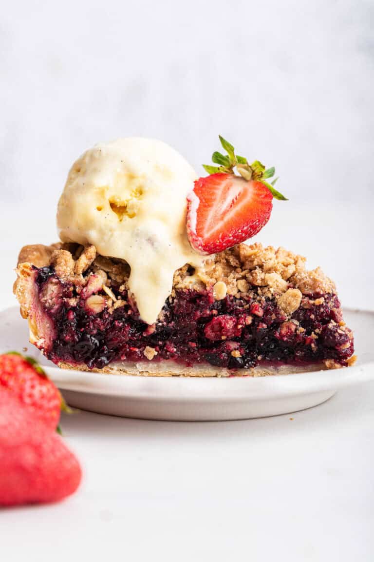 Side view of triple berry pie with ice cream and a berry.