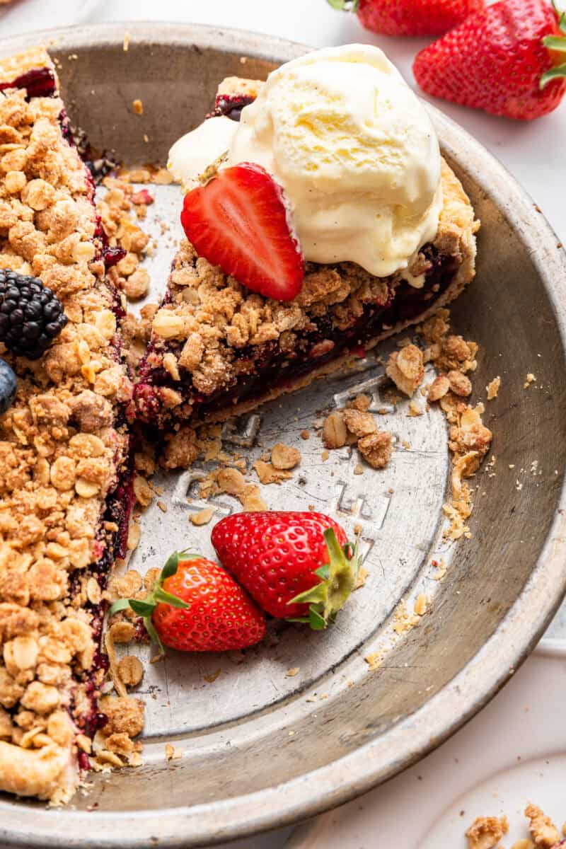 Single slice of pie cut from rest with ice cream and berries in pan.