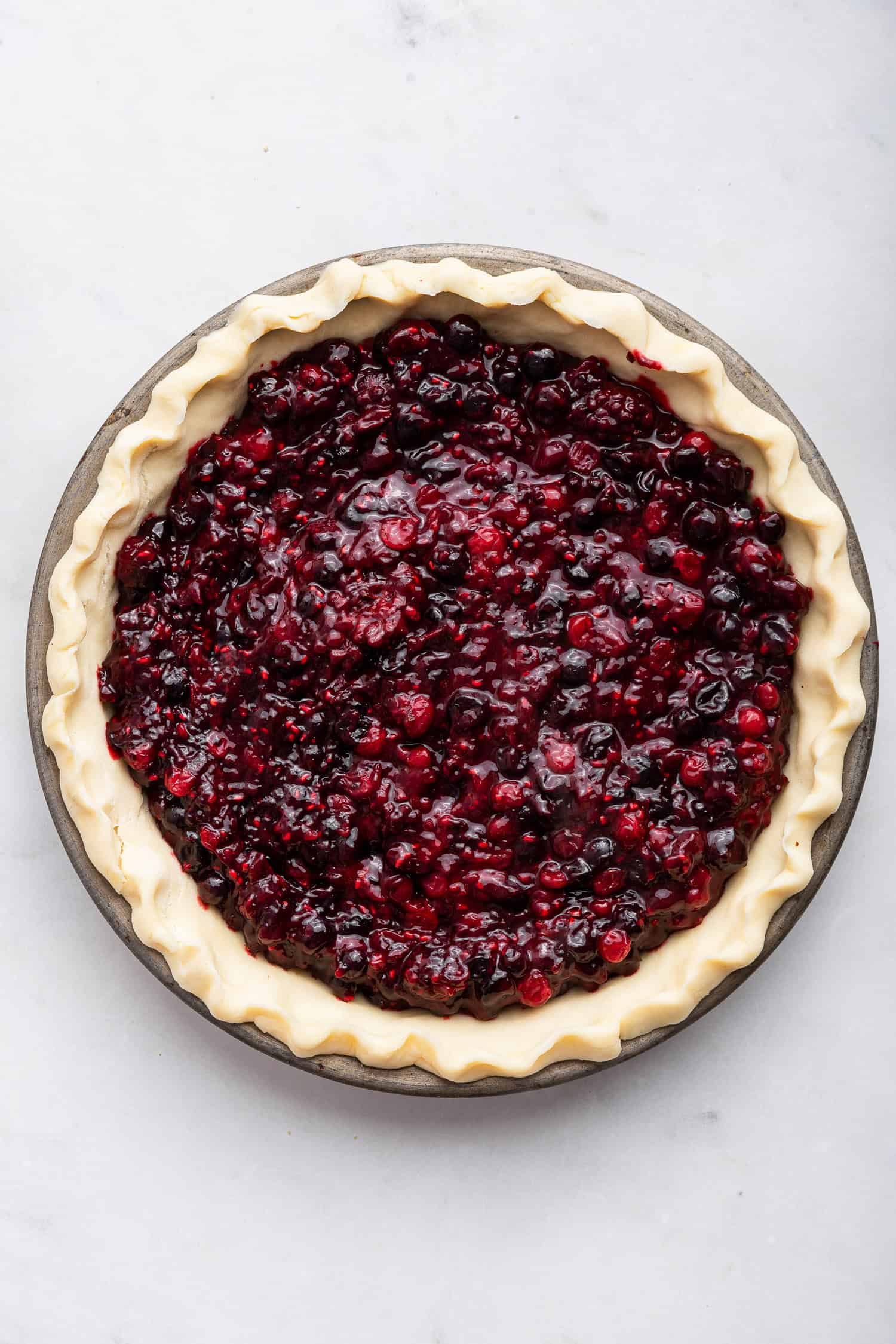 Filled pie crust ready to top with crumble topping.