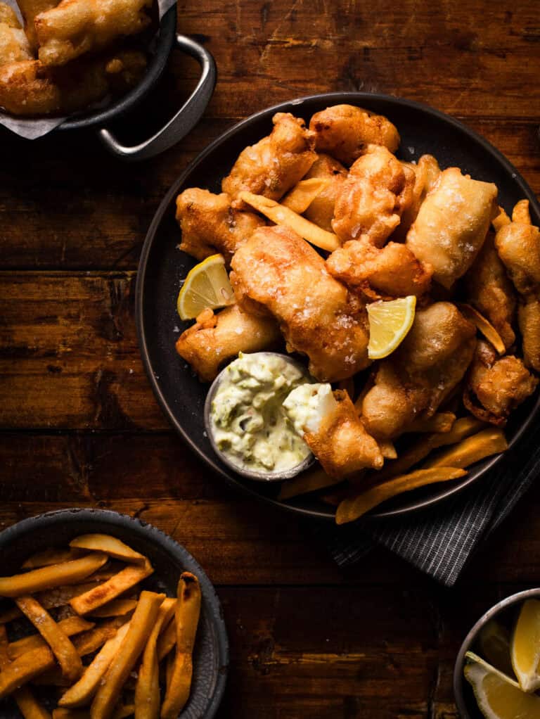 Fish fry with lemon and tartar and bowl of fries on side.