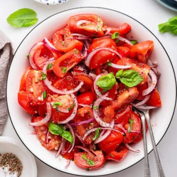 White bowl of Italian tomato salad with onions and basil and two forks.