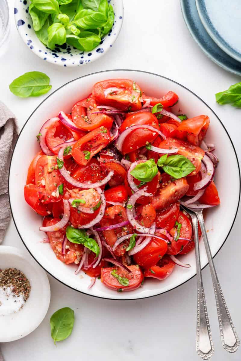 White bowl of Italian tomato salad with onions and basil and two forks.