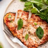 Eggplant pizzaiola with basil and side salad on plate.