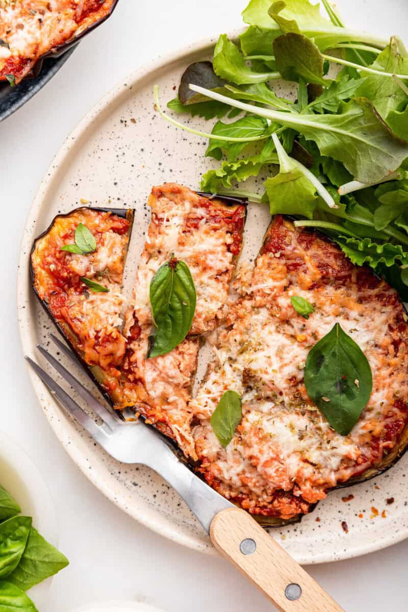 Eggplant pizzaiola with basil and side salad on plate.