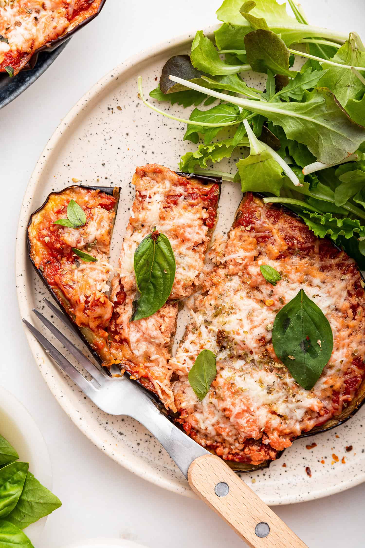 Eggplant pizzaiola with basil and side salad on plate.