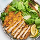 Oven fried chicken cutlets on a white dish with lettuce and lemon.