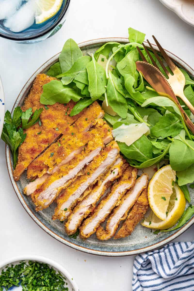 Oven fried chicken cutlets on a white dish with lettuce and lemon.