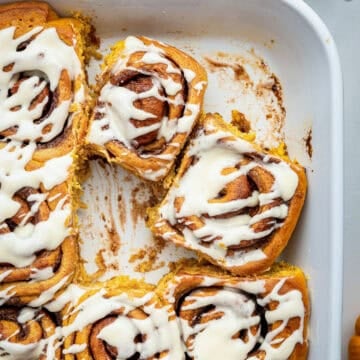 Frosting pumpkin rolls in white baking dish.