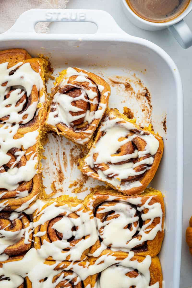 Frosting pumpkin rolls in white baking dish.