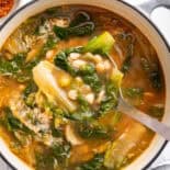 Escarole and beans soup in white pot with ladle.