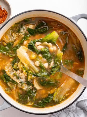 Escarole and beans soup in white pot with ladle.