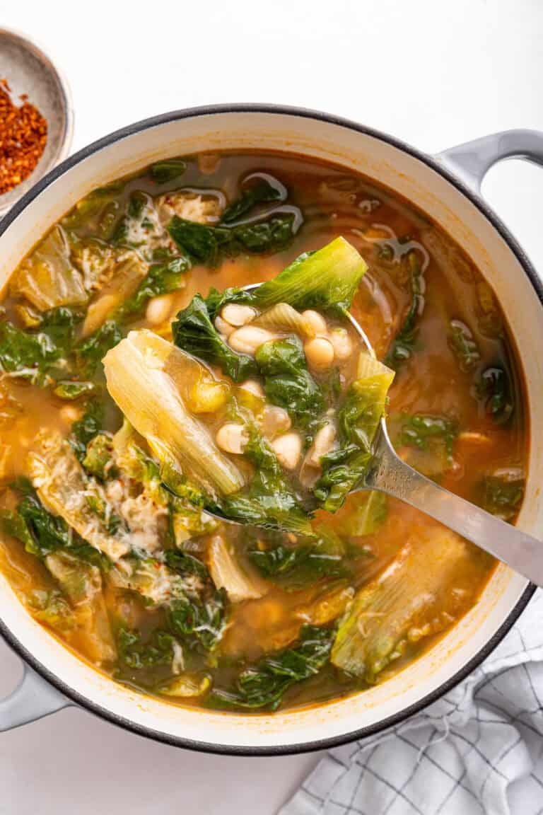 Escarole and beans soup in white pot with ladle.