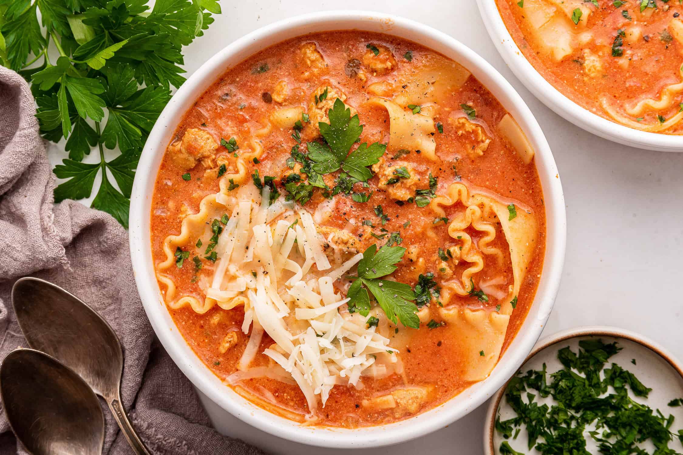 Bowl of lasagna soup with grated cheese and parsley.