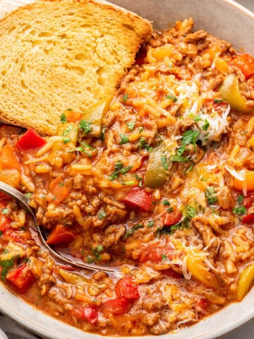 Stuffed pepper soup with bread in white bowl with spoon.