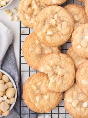 White chocolate macadamia nut cookies on wire reach with bowl of nuts.