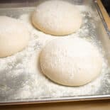 Three pizza dough balls dusted with flour on baking sheet.