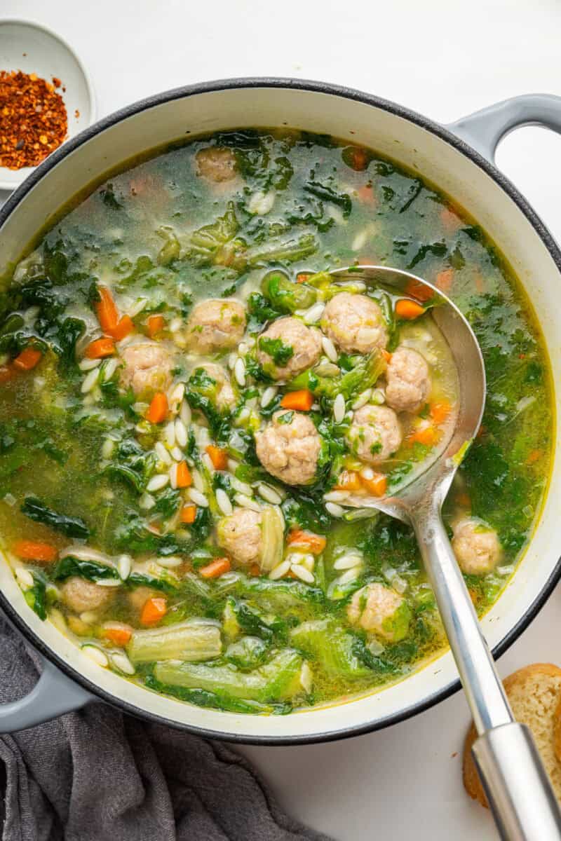 Italian wedding soup with mini meatballs, escarole and pasta in large white pot.