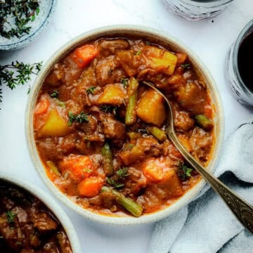 Bowl of beef stew with spoon and herbs.