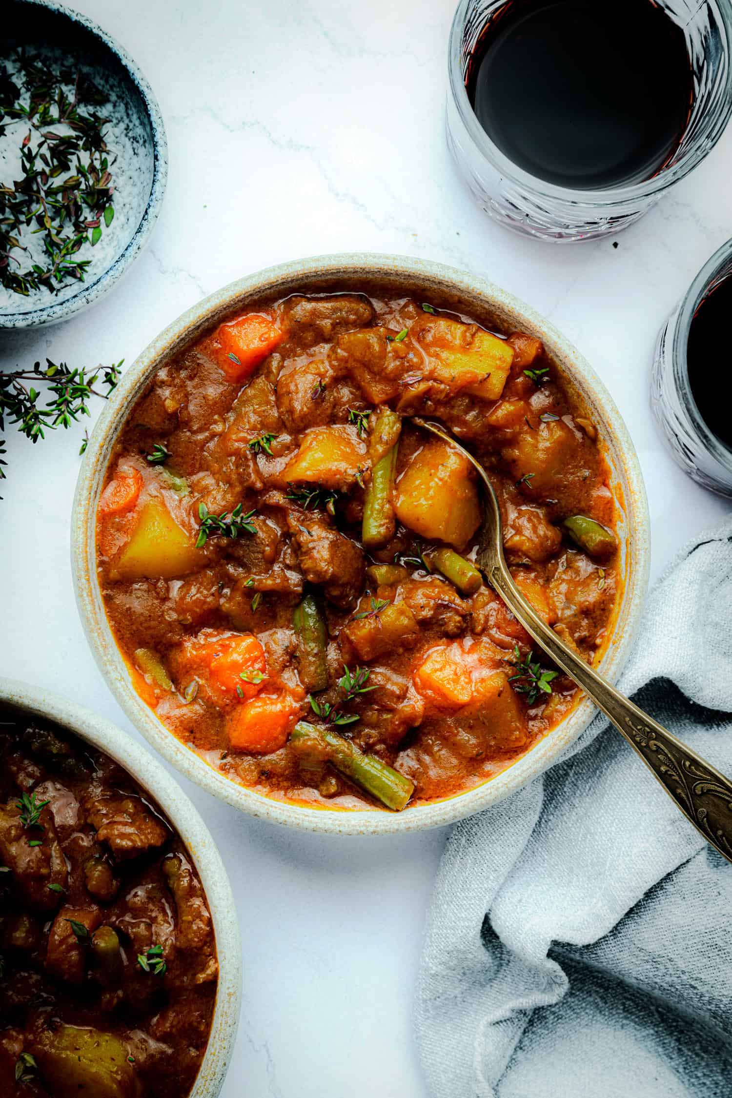 Bowl of beef stew with spoon and herbs. 