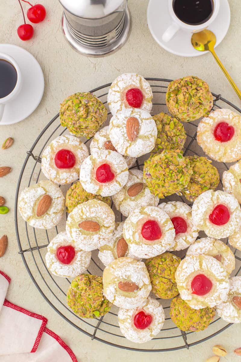 A variety of Sicilian almond cookies topped with cherries, almond or pistachios on a round wire rack.