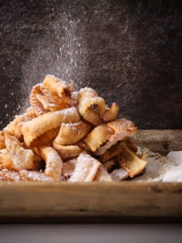 Dish of fried crostoli sprinkled with powdered sugar.