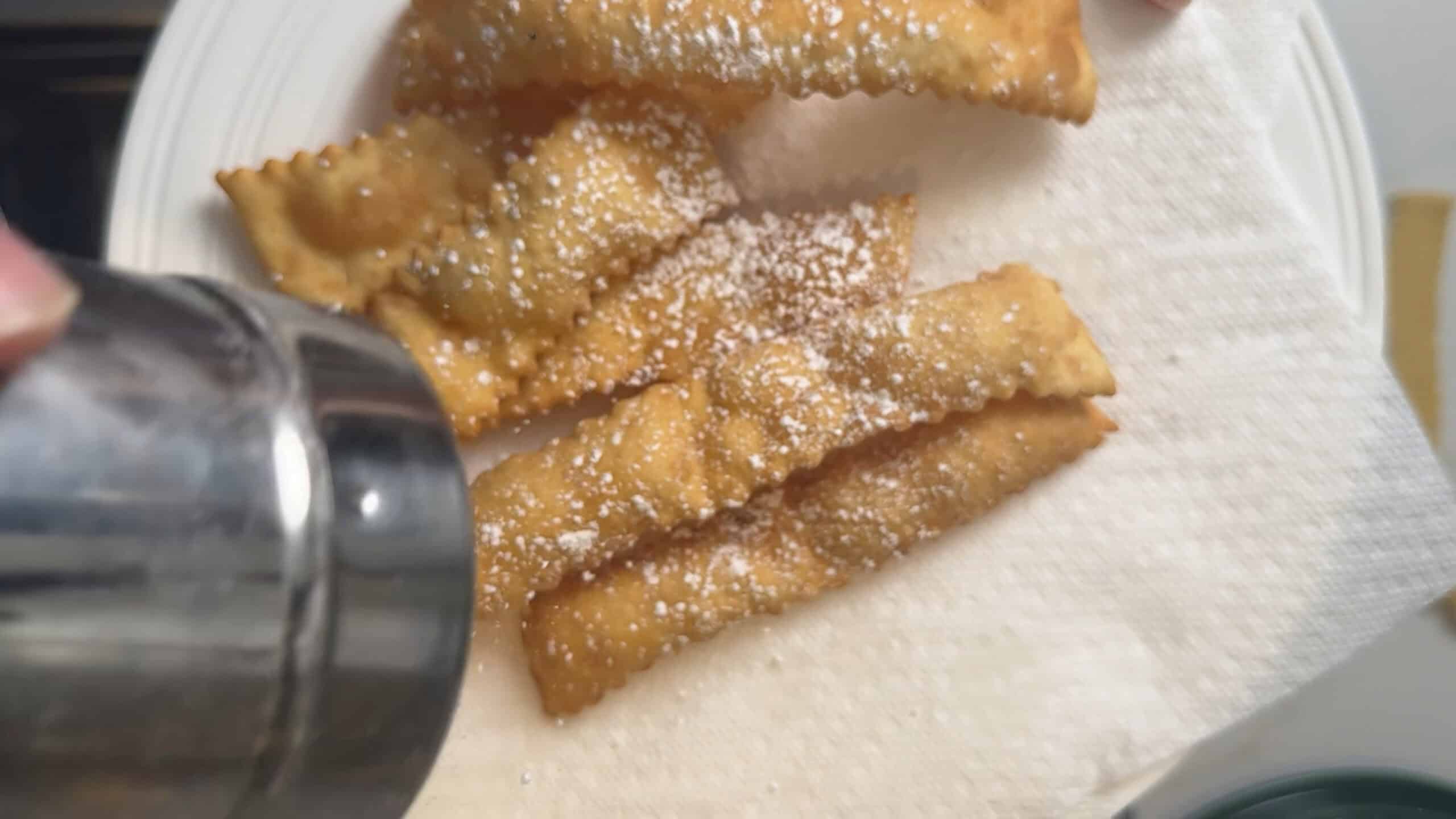 Dusting crostoli wit powdered sugar. 