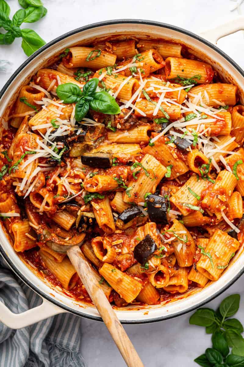 Pasta alla norma with wooden spoon in white pot.
