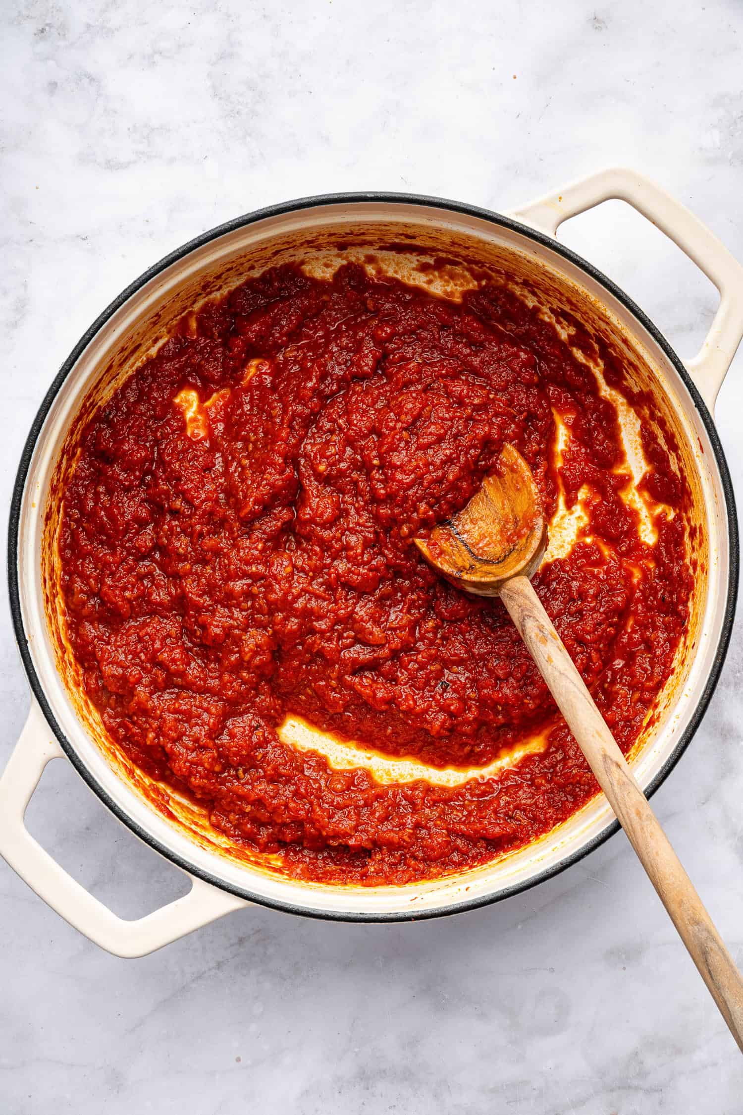 Tomato sauce thickened in white pot with spoon. 