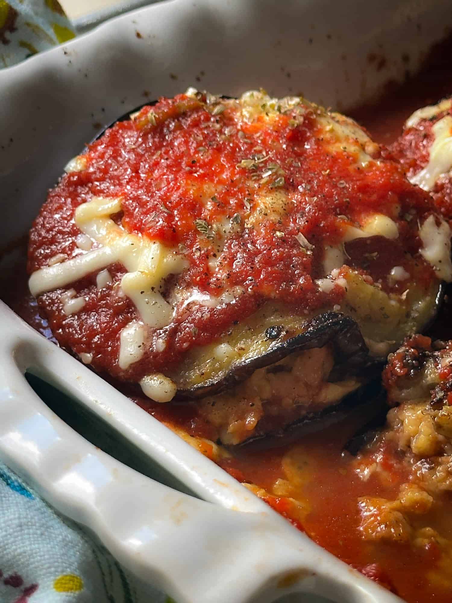 Baked stuffed eggplant with melted cheese, tomato sauce, and herbs in a white ceramic dish