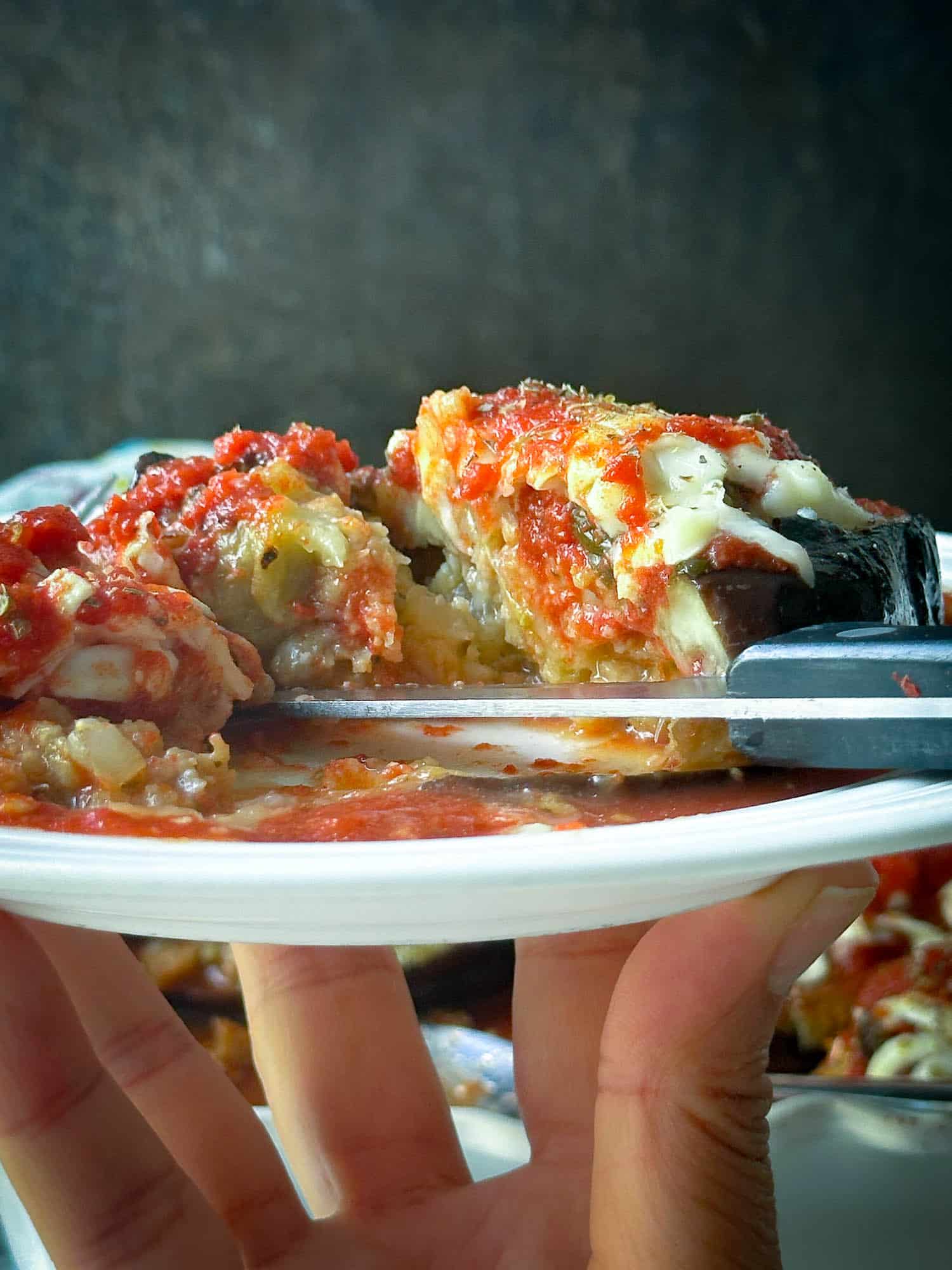 Savory eggplant stuffed slice with melted cheese and tomato sauce on white plate.