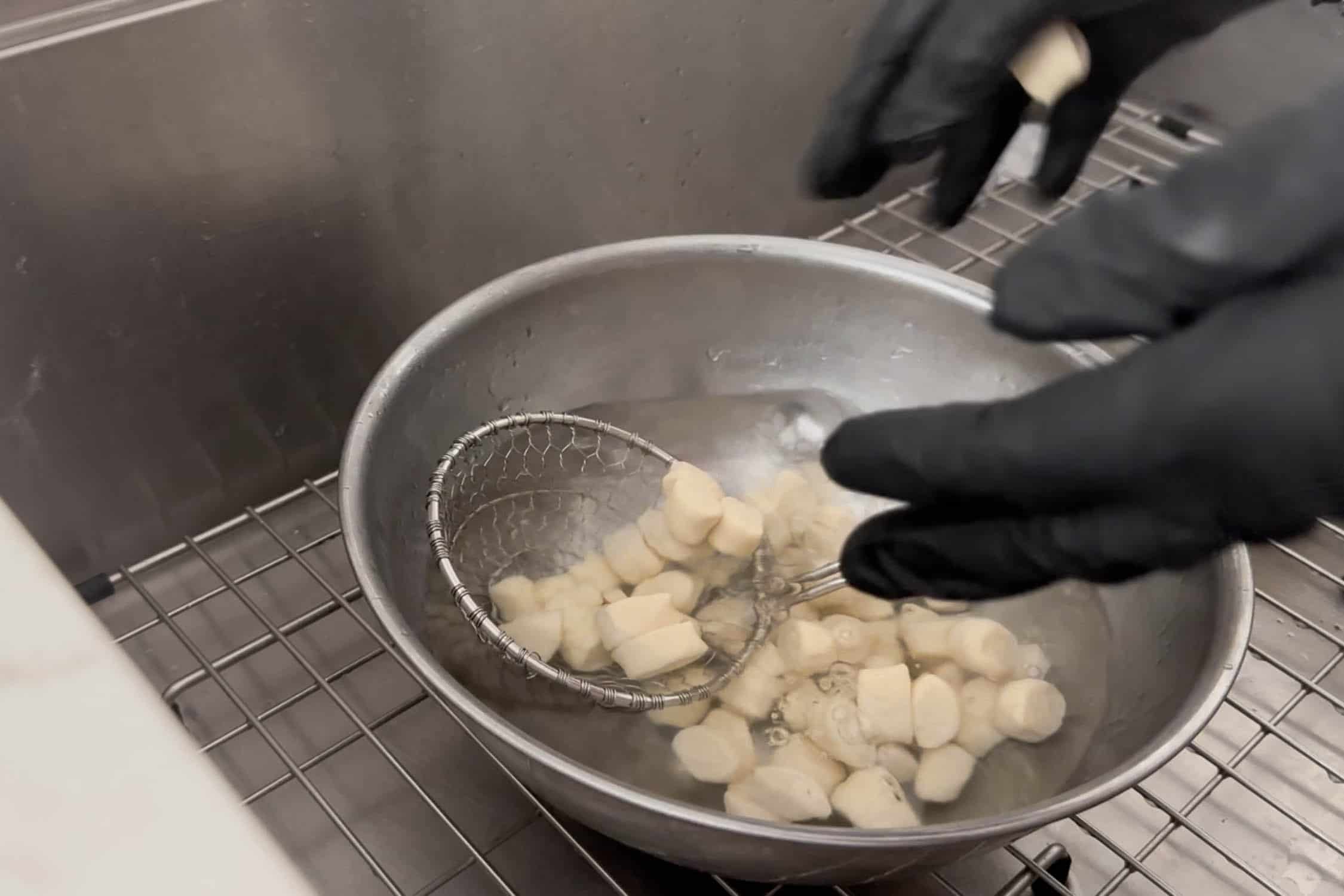 Preparing sourdough discard pretzel bites in a metal bowl with a lye bath and a strainer.