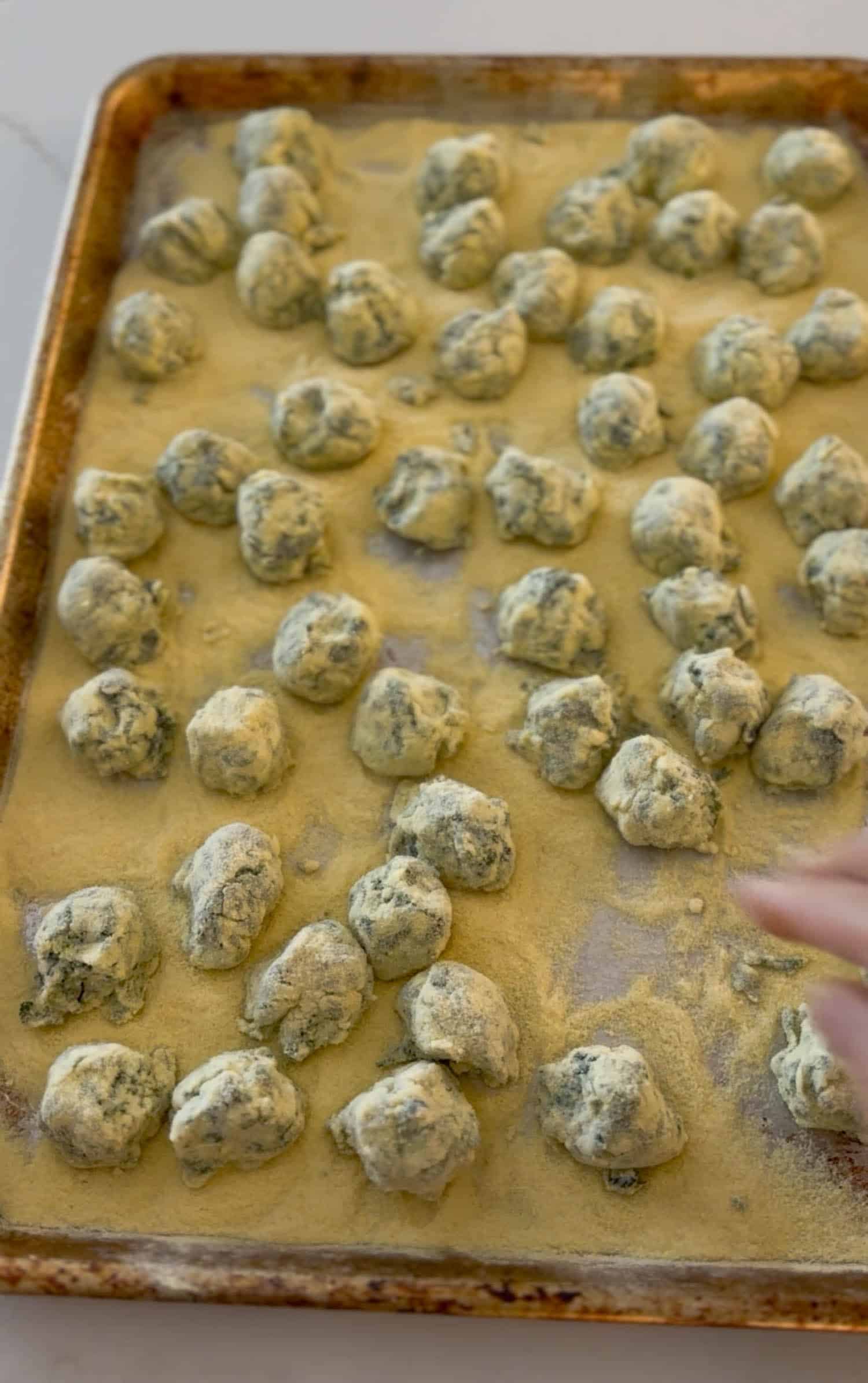 Raw gnudi dusted heavily with semolina on baking sheet ready to boil.