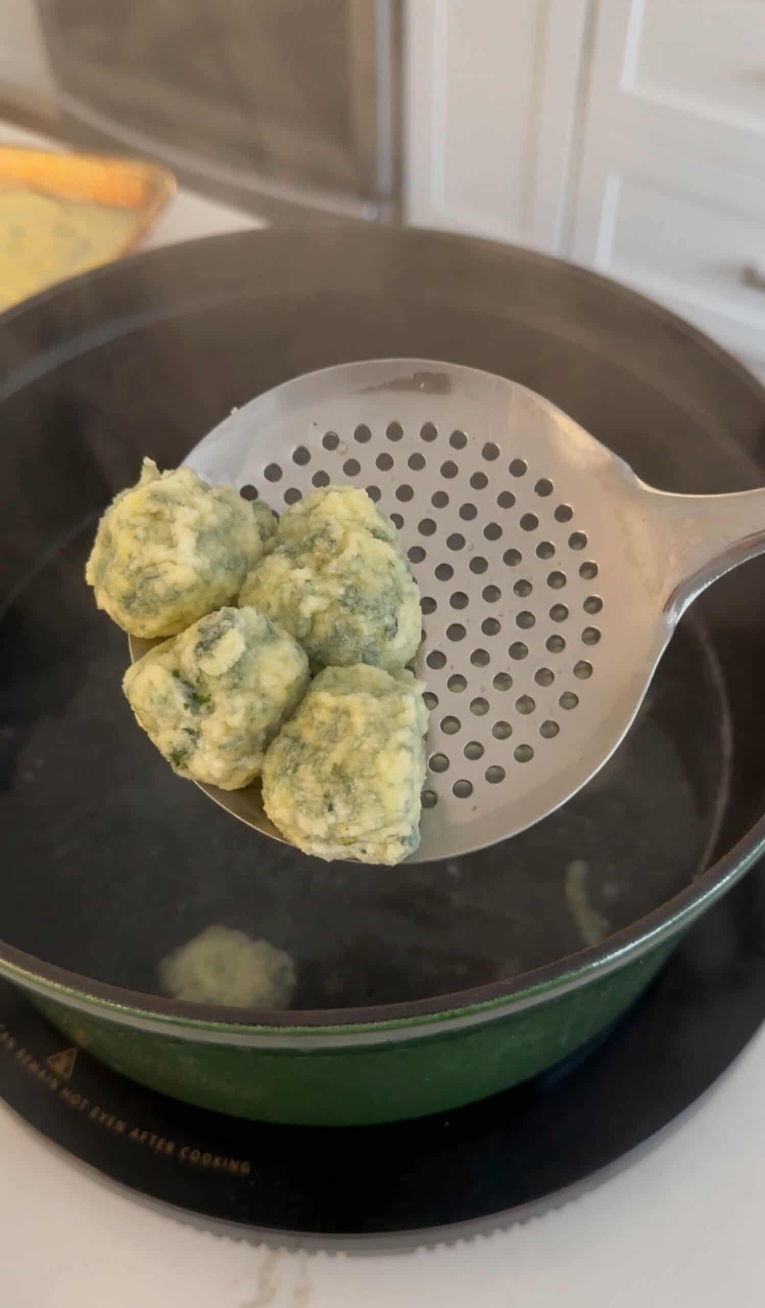 A few gnudi are shown on a perforated skimmer after boiling in dutch oven.