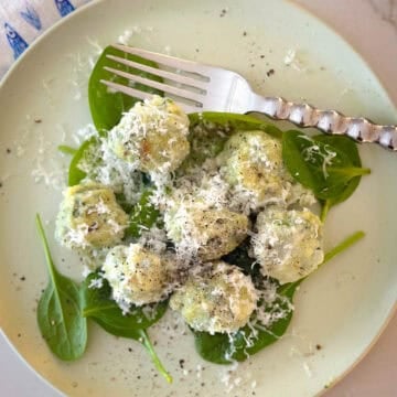 Top view of gnudi on plate with fresh spinach and fork.