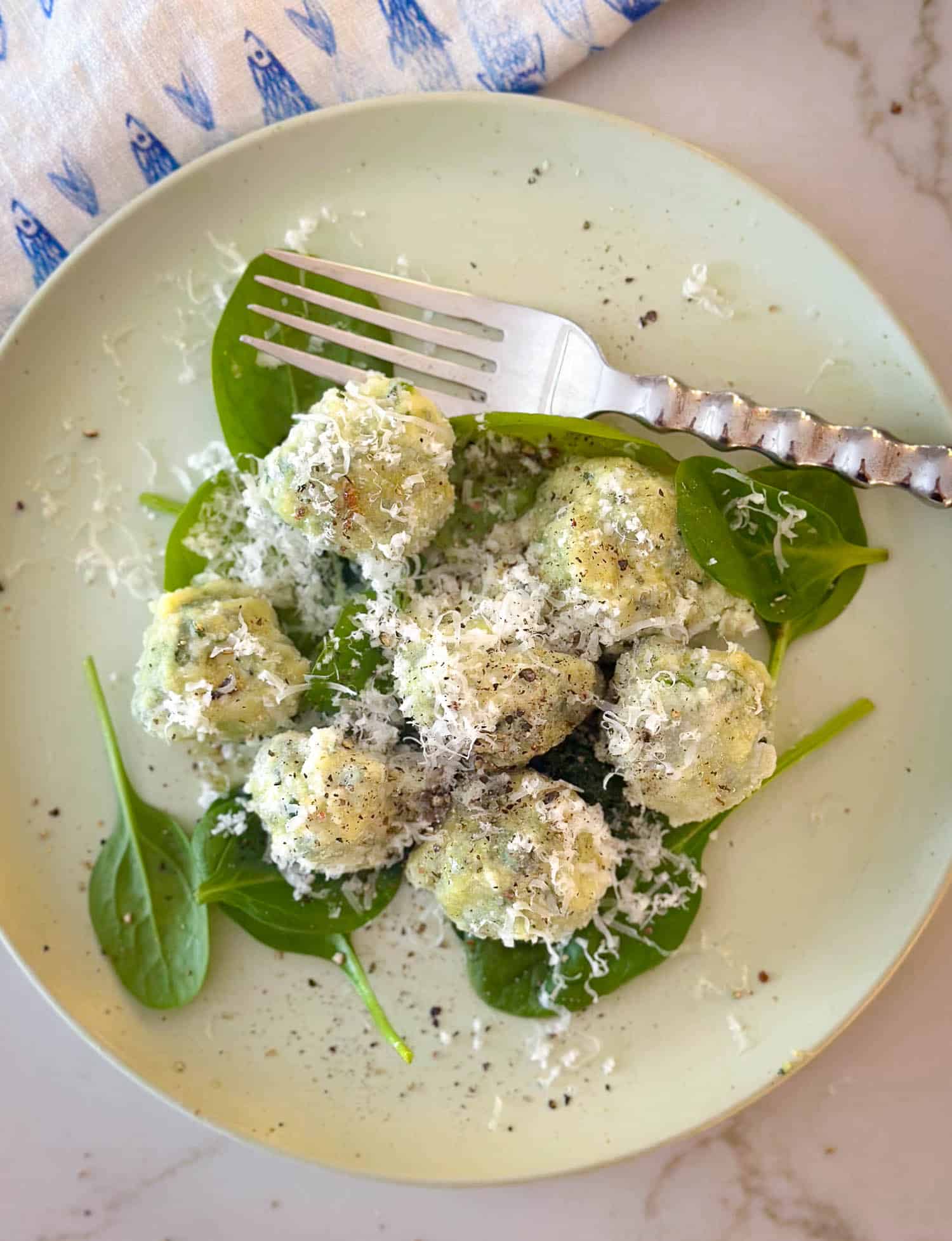 Top view of gnudi on plate with fresh spinach and fork.