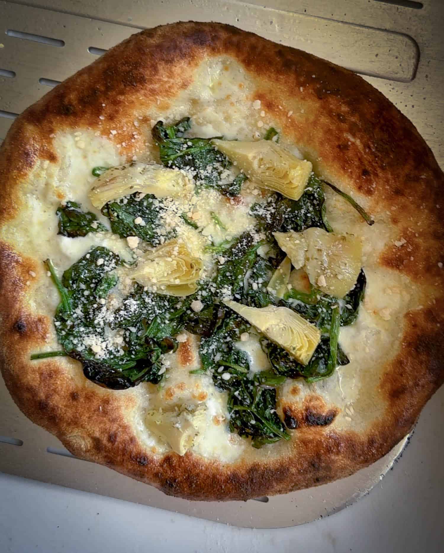 Top view of spinach and artichoke pizza baked in Ooni volt 2. 