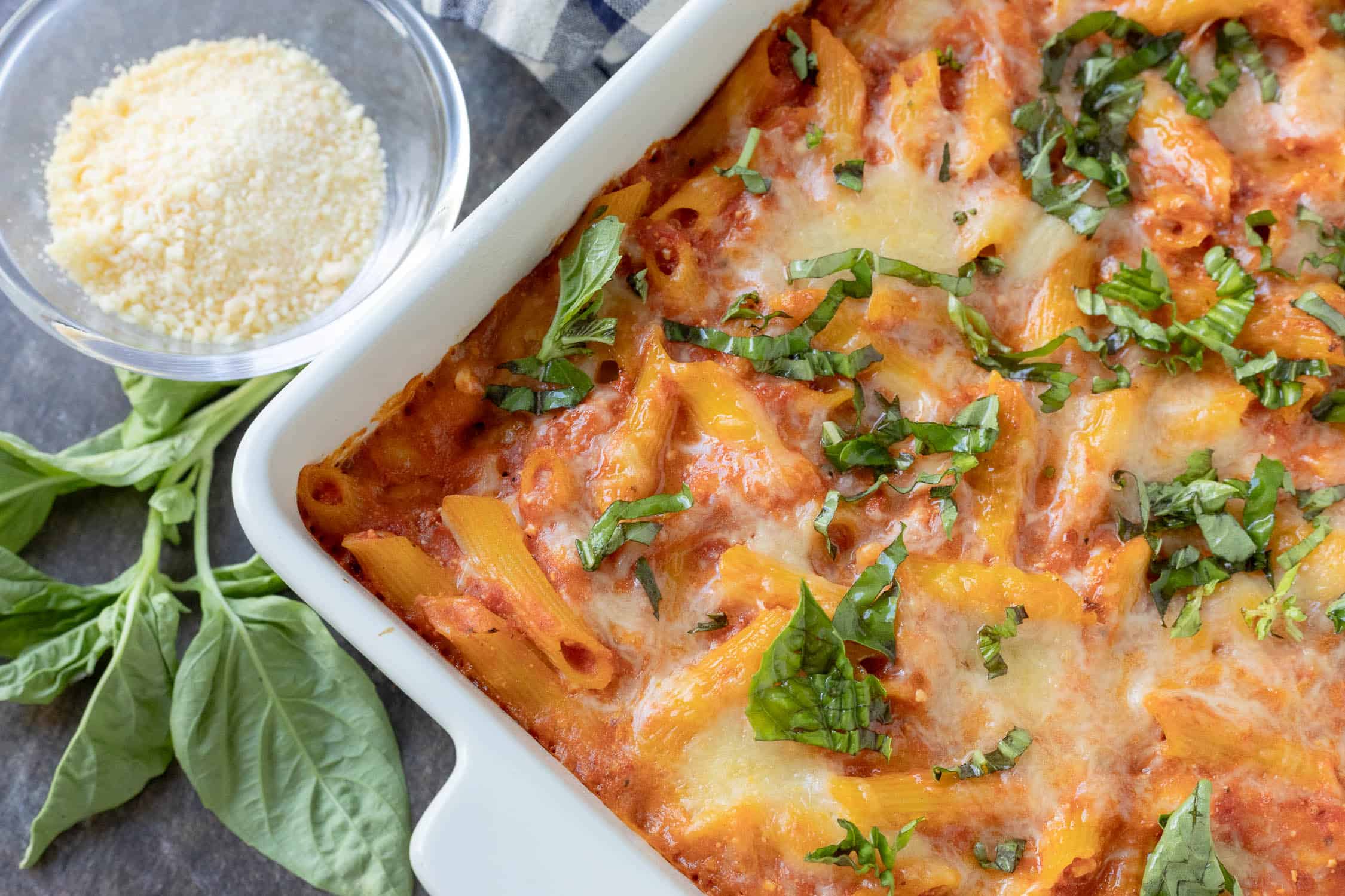 Corner view of baked ziti topped with basil. 