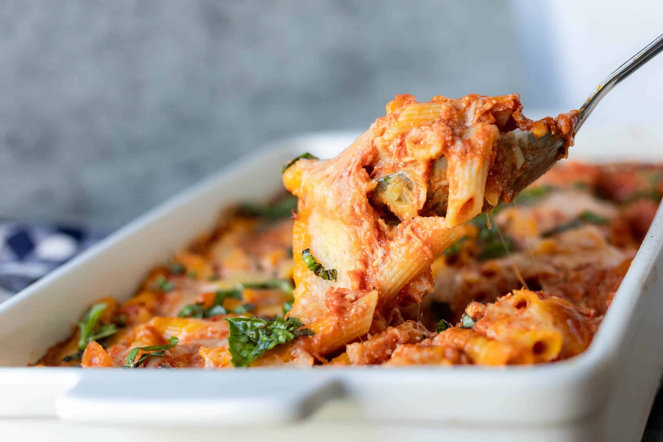 Spoon full of baked ziti being pulled out of pan. 