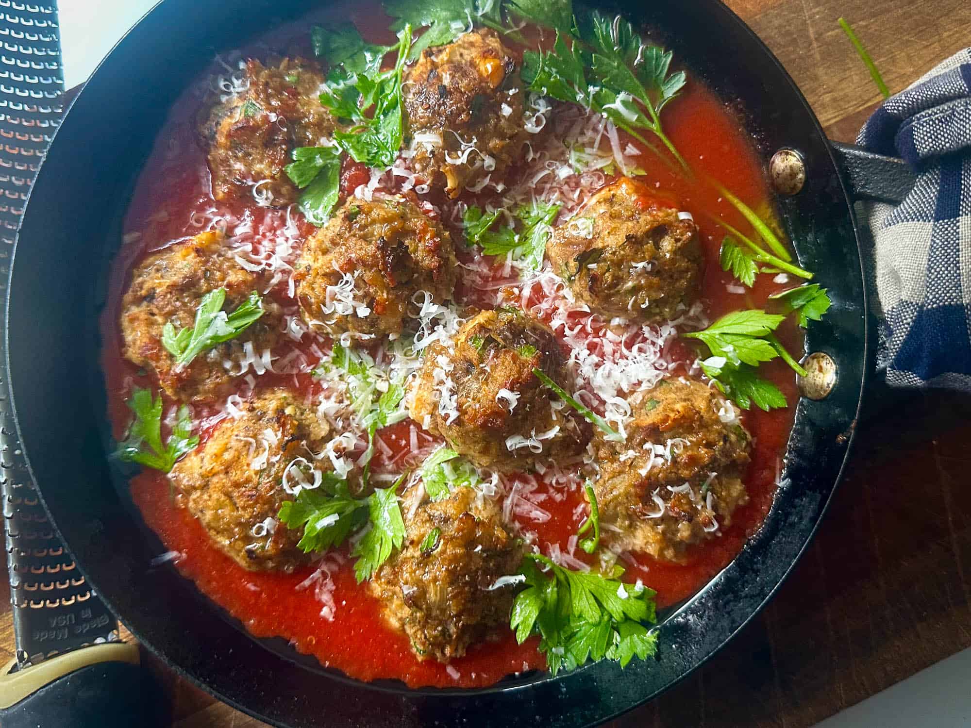 Overhead view of eggplant meatballs in pan with parsley, tomato sauce and grated cheese. 